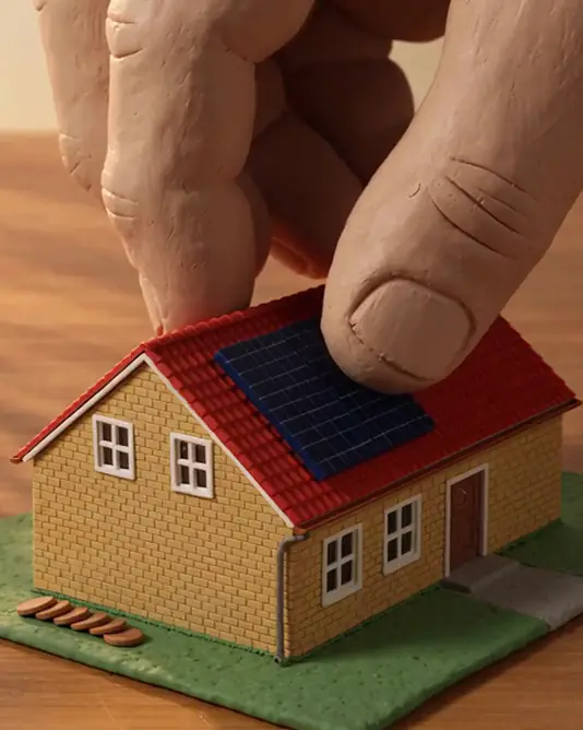 A muted loop of a clay hand lowering a dark blue solar panel onto a red tiled roof until it touches down