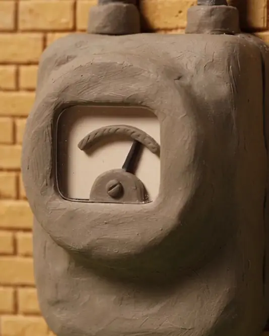 A muted clay loop of a clay electricity meter on a yellow brick wall, its needle swinging from the middle to the right